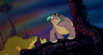 Movie still from “The Land Before Time” (1988), directed by Don Bluth – A group of animals that are standing in the dirt; Wide shot, Low angle