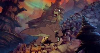 Movie still from “The Land Before Time” (1988), directed by Don Bluth – A dinosaur is walking through a rocky area; Wide shot, Low angle