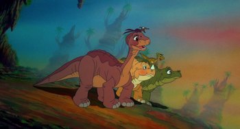 Movie still from “The Land Before Time” (1988), directed by Don Bluth – A group of three cartoon dinosaurs standing next to each other on top of a hill; Wide shot, High angle