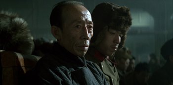 Movie still from “The Last Emperor” (1987), directed by Bernardo Bertolucci – Two men wearing winter coats and hats are sitting; Close Up shot, Over the shoulder angle