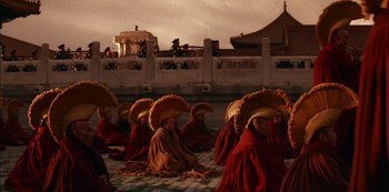 Movie still from “The Last Emperor” (1987), directed by Bernardo Bertolucci – A group of monks sitting on the ground with hats on their heads; Wide shot, High angle