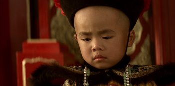 Movie still from “The Last Emperor” (1987), directed by Bernardo Bertolucci – A young boy wearing a hat and a necklace; Close Up shot, High angle