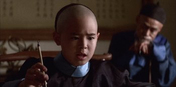 Movie still from “The Last Emperor” (1987), directed by Bernardo Bertolucci – A young boy with a shaved head is sitting in a chair; Close Up shot, High angle