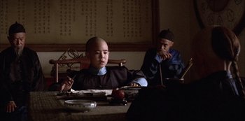 Movie still from “The Last Emperor” (1987), directed by Bernardo Bertolucci – A man sitting at a table in front of another man; Medium shot, Low angle