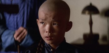 Movie still from “The Last Emperor” (1987), directed by Bernardo Bertolucci – A young boy with a bald head and a braid; Close Up shot, High angle