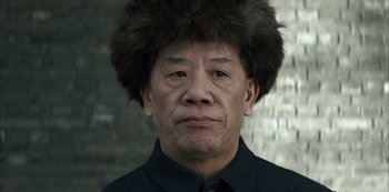 Movie still from “The Last Emperor” (1987), directed by Bernardo Bertolucci – An older man with an afro wearing a black shirt; Close Up shot, Low angle