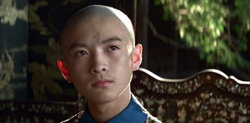 Movie still from “The Last Emperor” (1987), directed by Bernardo Bertolucci – A young man with a shaved head is posing for a picture; Close Up shot, Low angle