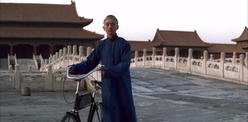 Movie still from “The Last Emperor” (1987), directed by Bernardo Bertolucci – A man standing next to a bicycle on a street; Medium shot, Low angle