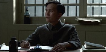 Movie still from “The Last Emperor” (1987), directed by Bernardo Bertolucci – A man sitting at a table in a room; Medium shot, Low angle