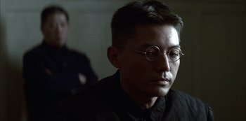 Movie still from “The Last Emperor” (1987), directed by Bernardo Bertolucci – A man wearing glasses and a black shirt; Close Up shot, Over the shoulder angle