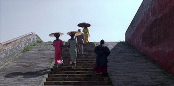 Movie still from “The Last Emperor” (1987), directed by Bernardo Bertolucci – A group of people walking up some steps with umbrellas; Extreme Wide shot, Low angle