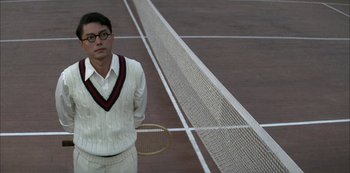 Movie still from “The Last Emperor” (1987), directed by Bernardo Bertolucci – A man standing on top of a tennis court holding a racquet; Medium shot, Over the shoulder angle