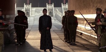 Movie still from “The Last Emperor” (1987), directed by Bernardo Bertolucci – A group of men standing next to each other on a sidewalk; Wide shot, Low angle