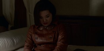 Movie still from “The Last Emperor” (1987), directed by Bernardo Bertolucci – A woman in a brown leather jacket sitting on a bed; Medium shot, High angle