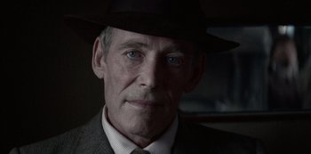 Movie still from “The Last Emperor” (1987), directed by Bernardo Bertolucci – An older man wearing a suit and a hat; Close Up shot, Over the shoulder angle