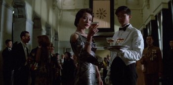 Movie still from “The Last Emperor” (1987), directed by Bernardo Bertolucci – A woman in a silver dress holding a tray of drinks; Medium shot, Low angle