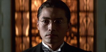 Movie still from “The Last Emperor” (1987), directed by Bernardo Bertolucci – A person wearing a suit and glasses; Close Up shot, Low angle