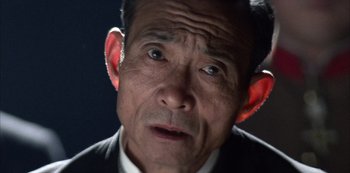 Movie still from “The Last Emperor” (1987), directed by Bernardo Bertolucci – An older man with ear plugs in his ears; Extreme Close Up shot, High angle
