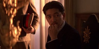 Movie still from “The Last Emperor” (1987), directed by Bernardo Bertolucci – A man in a suit and tie holding a book in his hand; Close Up shot, Low angle