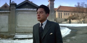 Movie still from “The Last Emperor” (1987), directed by Bernardo Bertolucci – A man in a suit and tie standing in front of a building; Close Up shot, Low angle