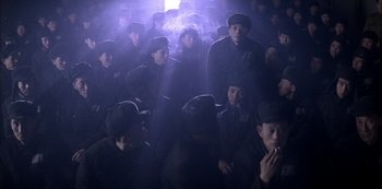 Movie still from “The Last Emperor” (1987), directed by Bernardo Bertolucci – A group of people in a dark room smoking; Wide shot, High angle
