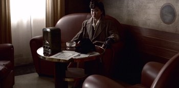 Movie still from “The Last Emperor” (1987), directed by Bernardo Bertolucci – A woman sitting at a table in a room; Medium shot, High angle