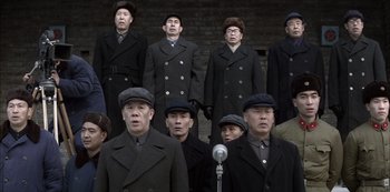 Movie still from “The Last Emperor” (1987), directed by Bernardo Bertolucci – A group of men standing next to each other in black coats; Medium shot, High angle