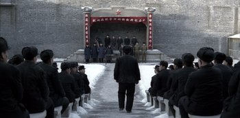 Movie still from “The Last Emperor” (1987), directed by Bernardo Bertolucci – A group of people sitting in front of a stage; Extreme Wide shot, High angle