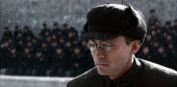 Movie still from “The Last Emperor” (1987), directed by Bernardo Bertolucci – A man with glasses and a hat is looking to his left; Close Up shot, Over the shoulder angle