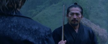 Movie still from “The Last Samurai” (2003), directed by Edward Zwick – A man holding a wooden stick while standing next to another man; Close Up shot, Over the shoulder angle