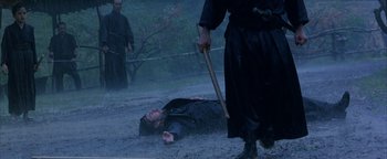 Movie still from “The Last Samurai” (2003), directed by Edward Zwick – A man is lying on the ground while another man holds a cane; Wide shot, Over the shoulder angle