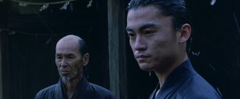Movie still from “The Last Samurai” (2003), directed by Edward Zwick – A man with a shaved head is standing next to another man with a shaved head; Close Up shot, Low angle