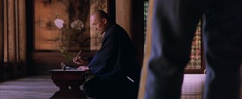 Movie still from “The Last Samurai” (2003), directed by Edward Zwick – A man sitting at a table writing on a piece of paper; Medium shot, Low angle