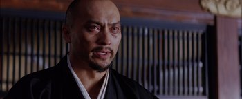 Movie still from “The Last Samurai” (2003), directed by Edward Zwick – A man with a shaved head wearing a black robe; Close Up shot, Over the shoulder angle