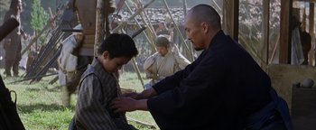 Movie still from “The Last Samurai” (2003), directed by Edward Zwick – A man and a boy are tying a tie; Medium shot, Over the shoulder angle