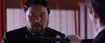 Movie still from “The Last Samurai” (2003), directed by Edward Zwick – A man with a beard and mustache wearing a suit and tie; Close Up shot, Low angle