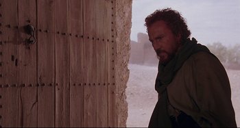 Movie still from “The Last Temptation of Christ” (1988), directed by Martin Scorsese – A man standing in front of a wooden door; Medium shot, Low angle