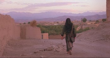 Movie still from “The Last Temptation of Christ” (1988), directed by Martin Scorsese – A woman walking down a dirt road with a bag; Wide shot, Low angle