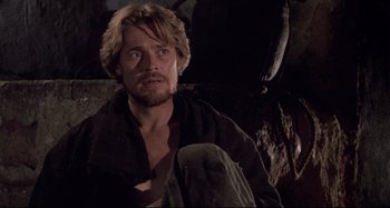 Movie still from “The Last Temptation of Christ” (1988), directed by Martin Scorsese – A person sitting on the ground near a wall; Close Up shot, Low angle