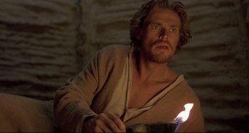 Movie still from “The Last Temptation of Christ” (1988), directed by Martin Scorsese – A man holding a lit candle in a cave setting; Close Up shot, Low angle