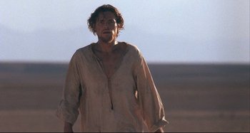 Movie still from “The Last Temptation of Christ” (1988), directed by Martin Scorsese – A man in a tan shirt is standing in the desert; Medium shot, Low angle