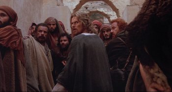 Movie still from “The Last Temptation of Christ” (1988), directed by Martin Scorsese – A group of men standing around a man in front of a wall; Medium shot, Over the shoulder angle