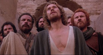 Movie still from “The Last Temptation of Christ” (1988), directed by Martin Scorsese – A group of men standing around a man in a white shirt; Medium shot, Low angle