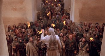 Movie still from “The Last Temptation of Christ” (1988), directed by Martin Scorsese – A crowd of people standing around a building with a man holding torches in his hand; Wide shot, High angle