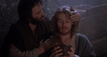 Movie still from “The Last Temptation of Christ” (1988), directed by Martin Scorsese – A man with long hair is holding a cup while a man with a beard is touching his head; Close Up shot, Over the shoulder angle