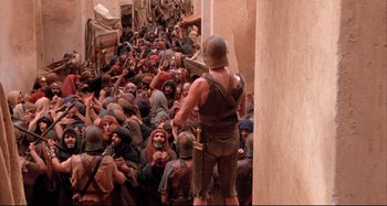 Movie still from “The Last Temptation of Christ” (1988), directed by Martin Scorsese – A crowd of people are gathered around a man in a helmet; Wide shot, High angle