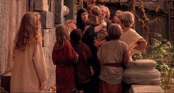 Movie still from “The Last Temptation of Christ” (1988), directed by Martin Scorsese – A group of people standing around each other near a stone wall; Medium shot, High angle