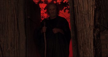 Movie still from “The Last Temptation of Christ” (1988), directed by Martin Scorsese – An old man with a cane standing in front of a red wall; Medium shot, Low angle