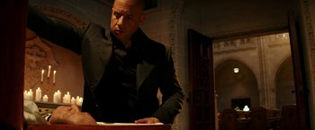 Movie still from “The Last Witch Hunter” (2015), directed by Breck Eisner – A bald man in a black jacket is standing at a table; Medium shot, Low angle