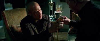 Movie still from “The Last Witch Hunter” (2015), directed by Breck Eisner – A bald man holding a glass of orange juice in his hand; Medium shot, Over the shoulder angle